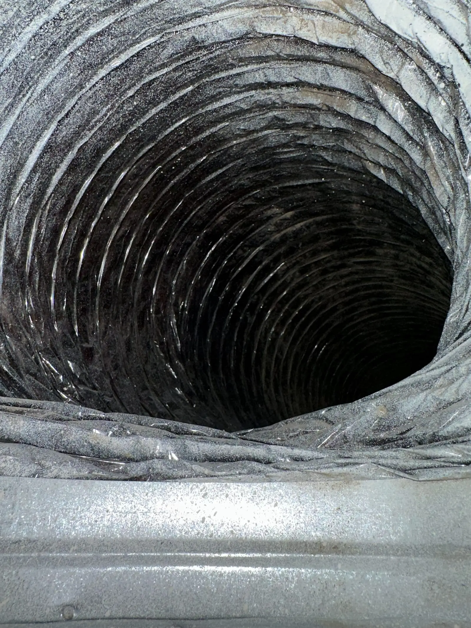 View down the length of a dusty flexible HVAC duct before cleaning