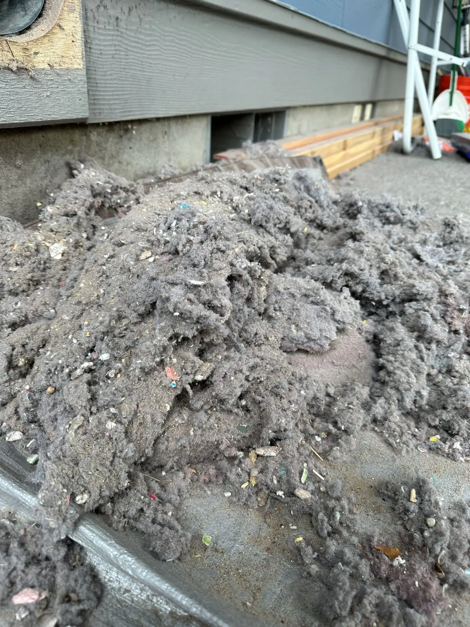 A heaped mound of dryer lint on the ground beside a house after a vent cleaning