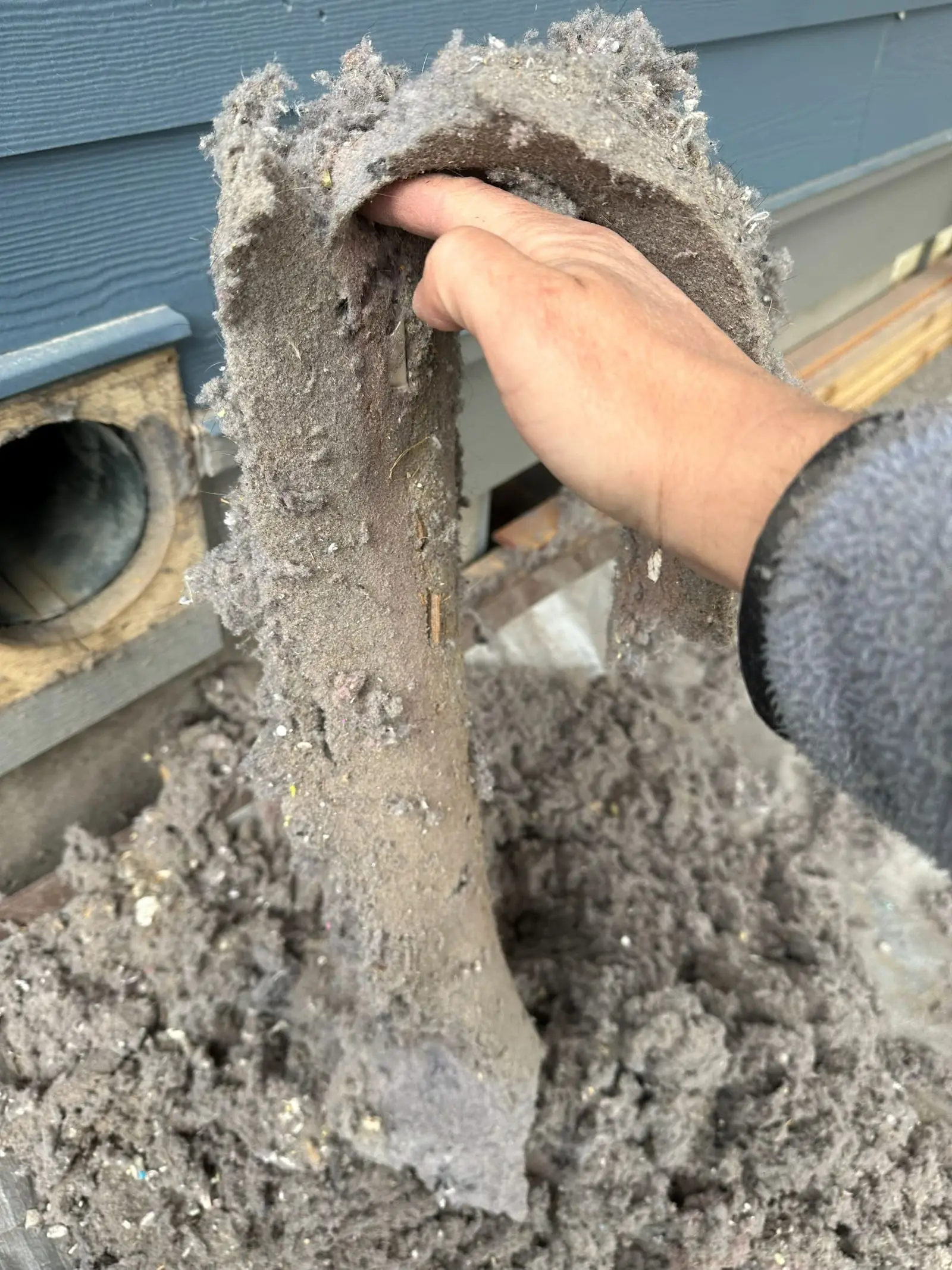 A hand holding a section of dryer duct packed solid with compacted lint