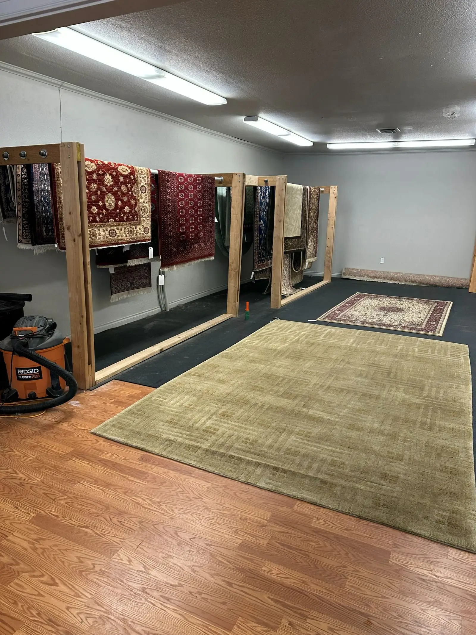 Area rugs laid out to dry on the floor of the rug cleaning facility, with drying racks along the wall